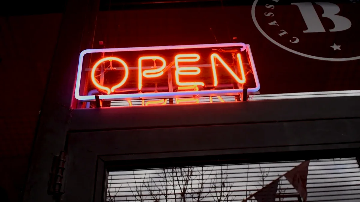 Fotograma del fashion film: cartel de neón rojo con la palabra OPEN